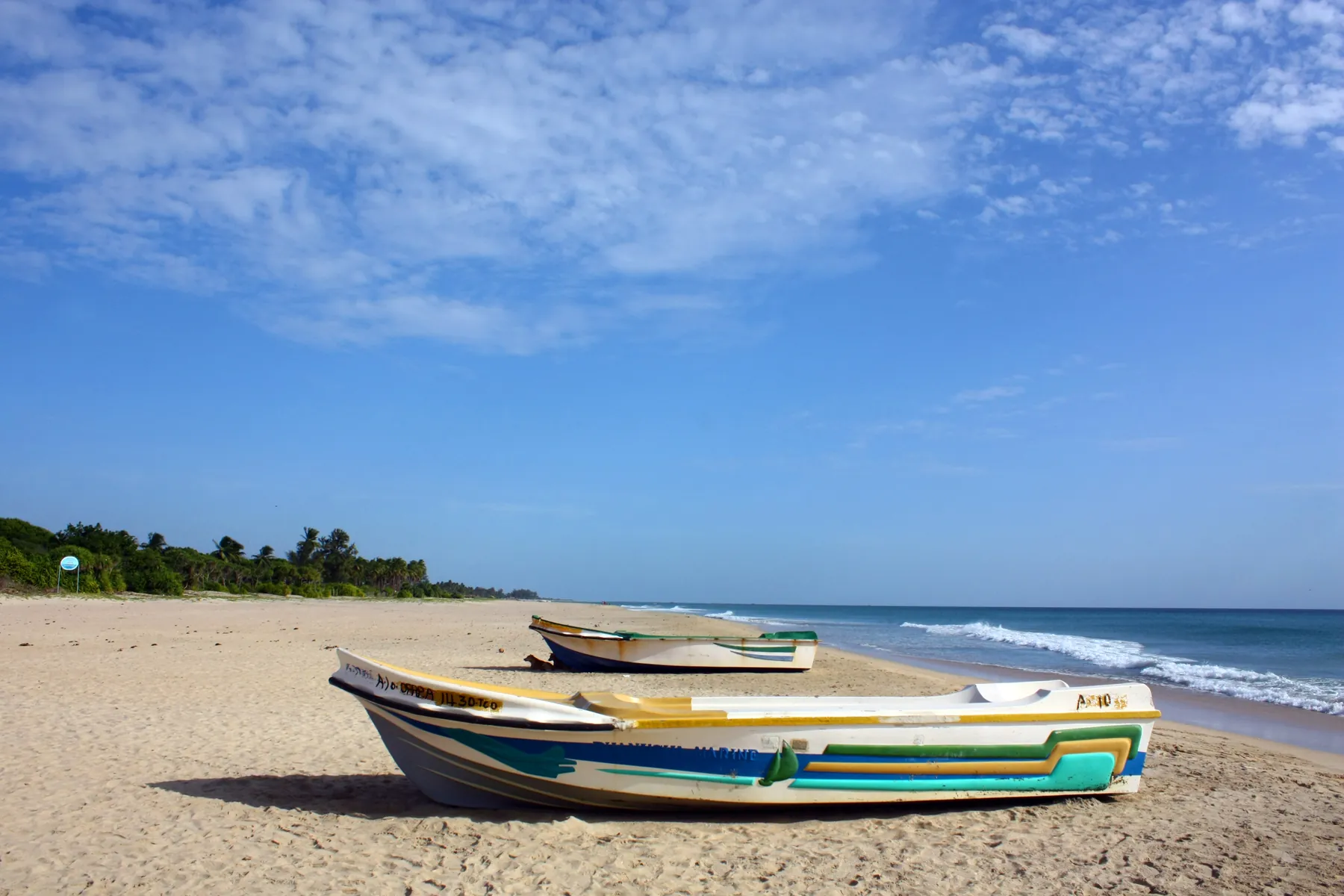 Painted fishing boats on the sand at Nilaveli Beach under a blue sky.