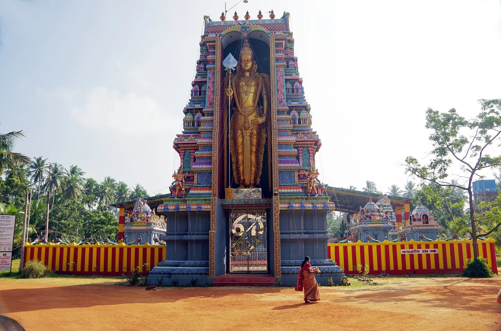 A brightly painted temple tower at Munneswaram near Chilaw, with a large gold Murugan statue in a central niche.