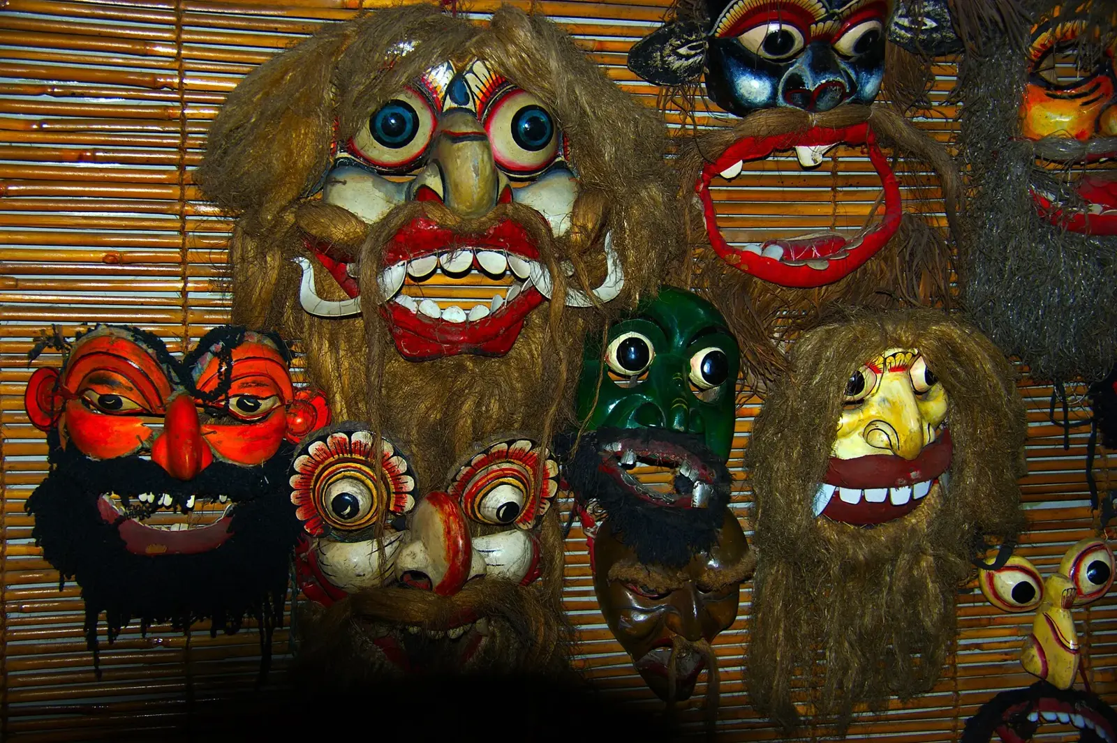 Brightly painted wooden masks with bulging eyes, bared teeth and fibre hair, hung on a bamboo blind in Ambalangoda.