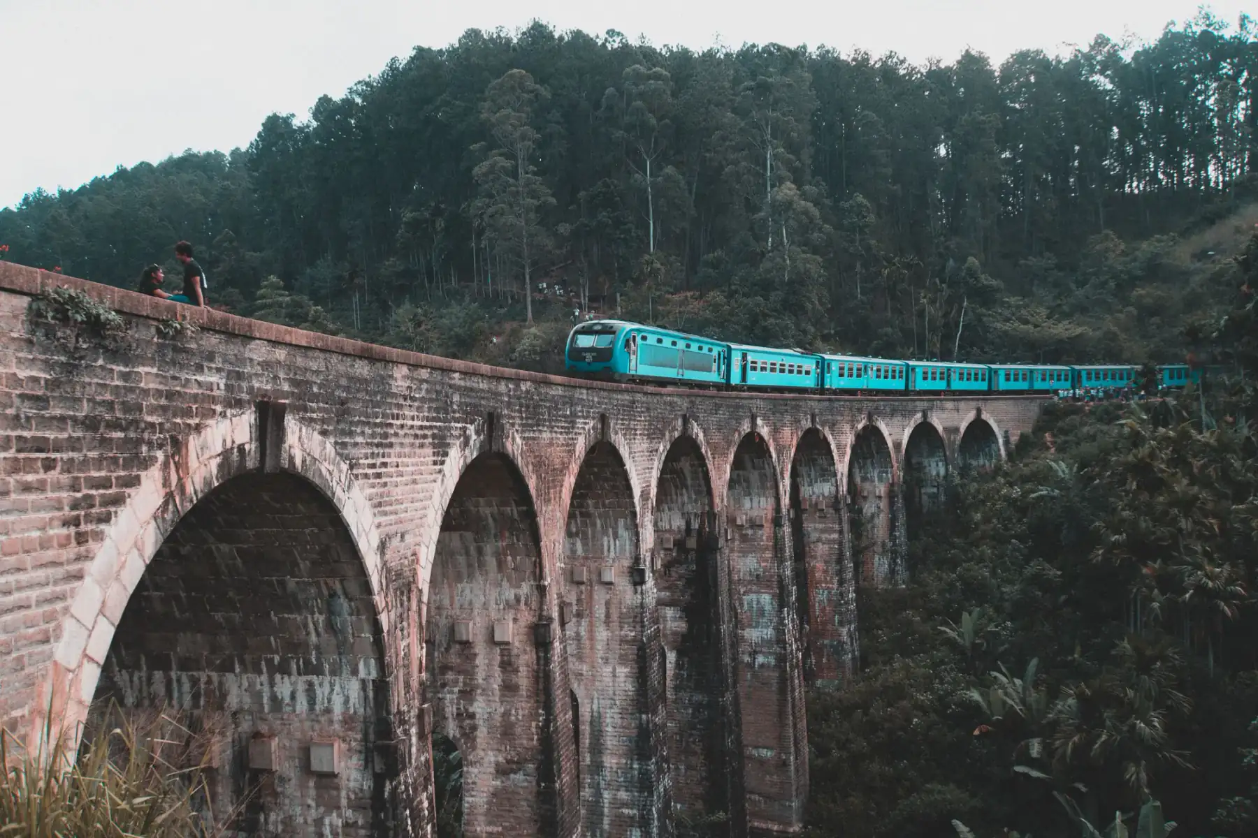 A blue hill-country train crossing the Nine Arch Bridge above dense jungle near Ella.